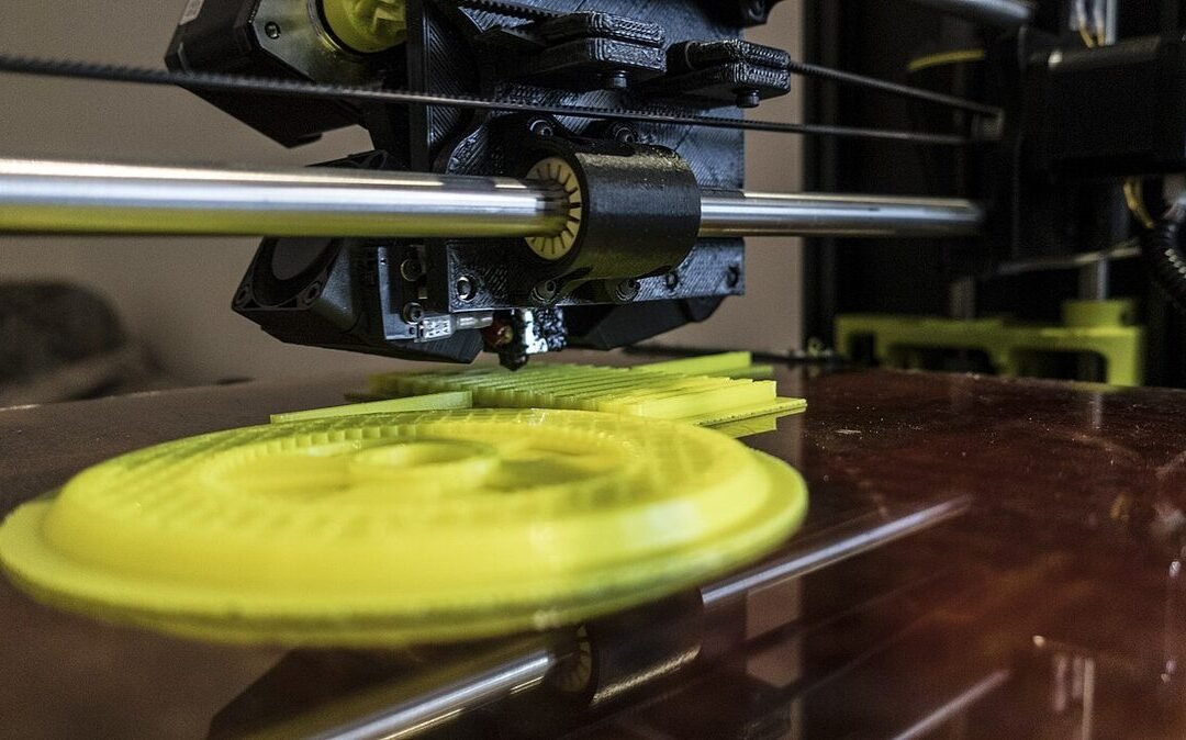 Druckkopf eines 3D-Druckers über einem gelben, ringförmigen Druckteil auf der Glasplatte