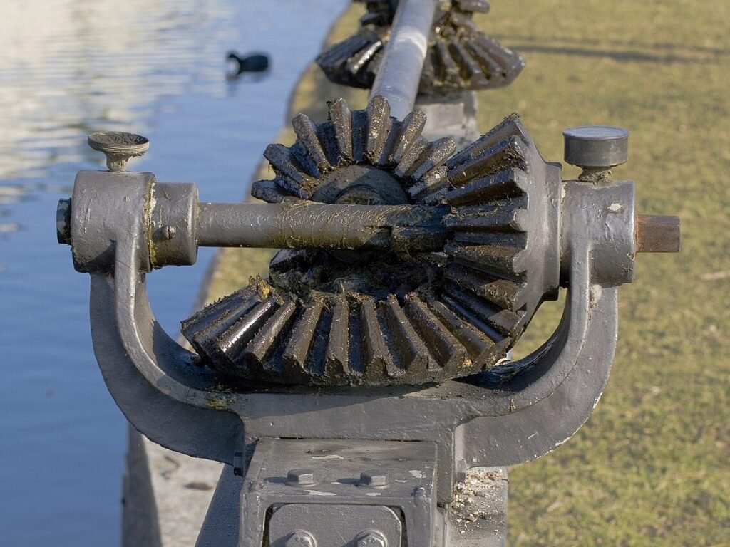 Zwei ineinandergreifende Kegelräder aus Gusseisen an einer Welle, im Hintergrund Wasser